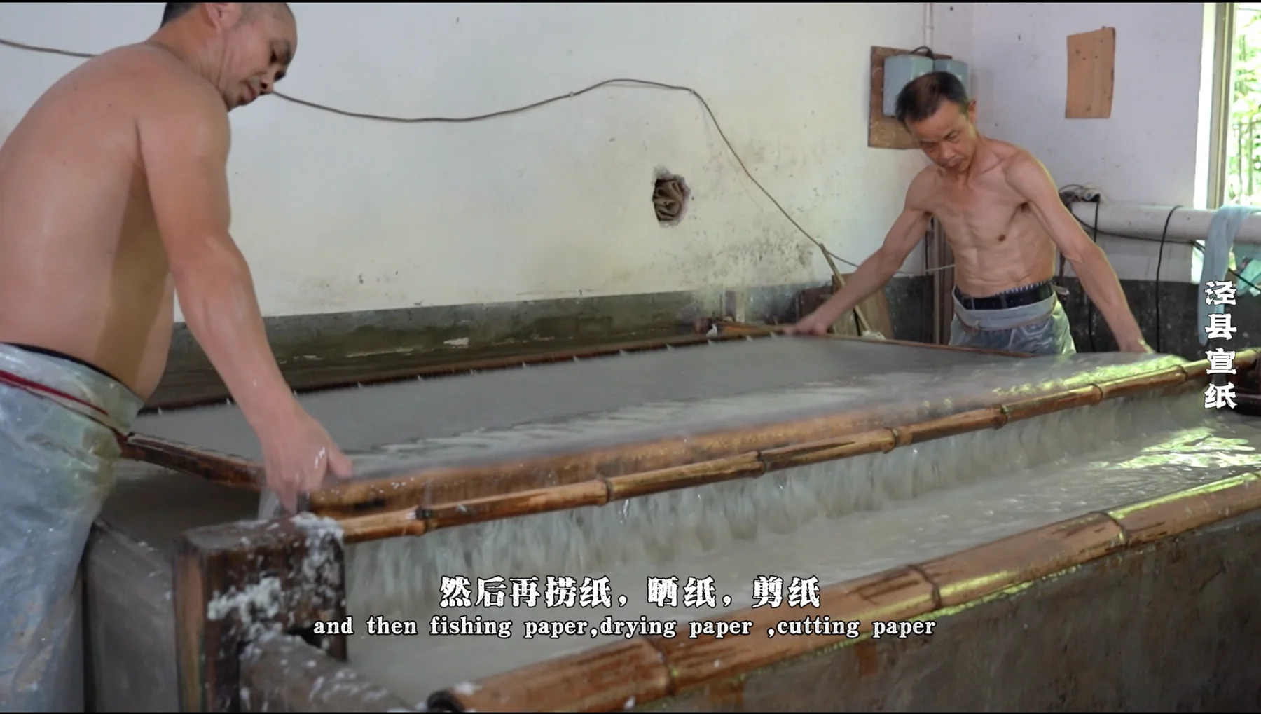 Two craftspeople lifting a large paper-making screen from a vat